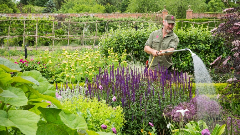 A gardener watering the garden in summer at Wimpole Estate, Cambridgeshire